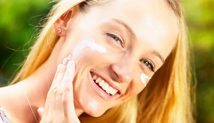 A woman applying sunscreen to her face.