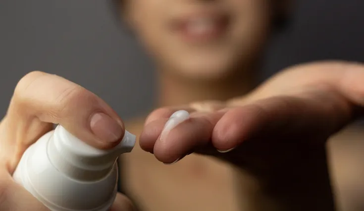 A closeup of a person applying a dab of Retinol to their finger from a pump bottle.