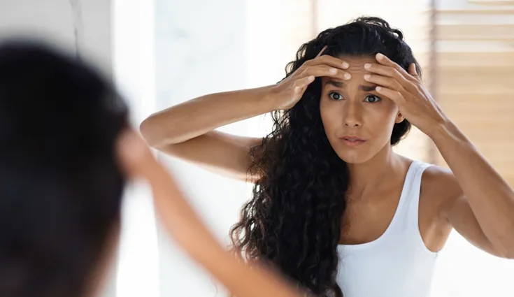 A woman examines her forehead for dehydration lines.