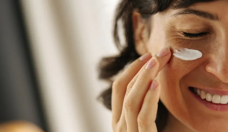 A woman applies a facial cream under her eyes