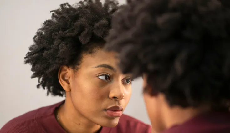 A black woman checks her skin in the mirror