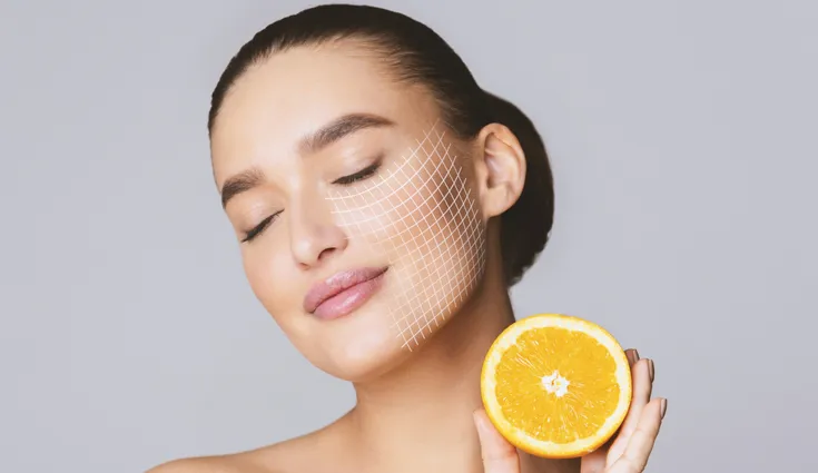 A woman poses with an orange next to her skin